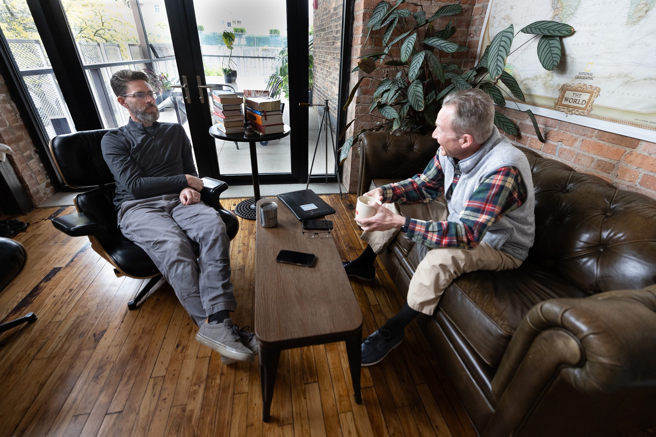 Two people in warm, focused conversation in the TalkLab studio, a world map and stacked books behind them